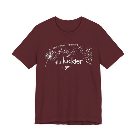 Front view of a maroon Bella Canvas t-shirt with a clever music-themed graphic. The design shows a stylized guitar headstock and musical notes above text that reads: ‘The more I practice, the luckier I get.’ Soft 100% cotton shirt perfect for musicians and music teachers.