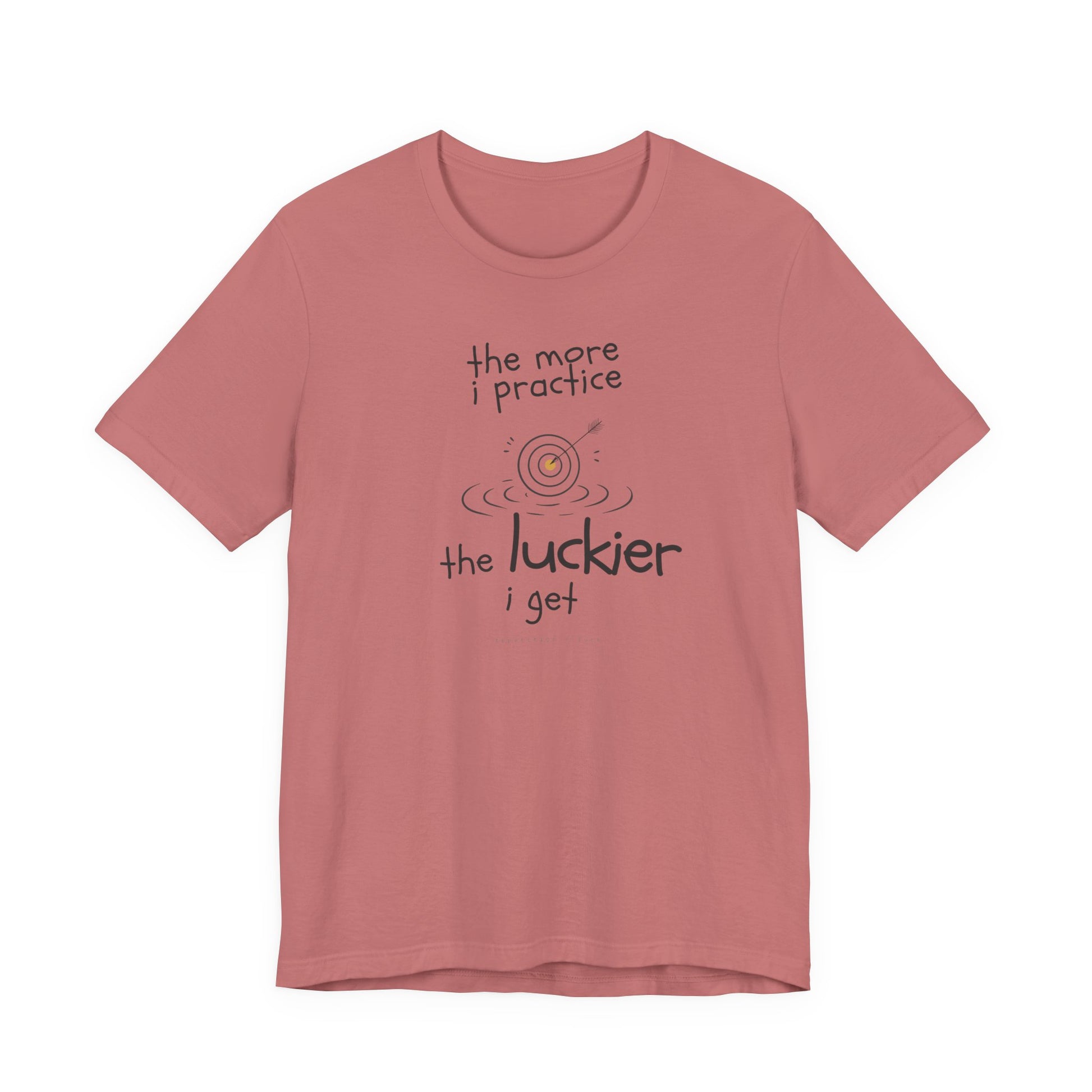 Minimalist motivational T-shirt design shown on a mauve coloured shirt: hand-drawn cream lettering reads “the more i practice” above a sketched bullseye with an arrow and small mustard center, ripple lines underneath, then larger text reads “the luckier i get” with tiny mono text below that says “repetition > luck.”