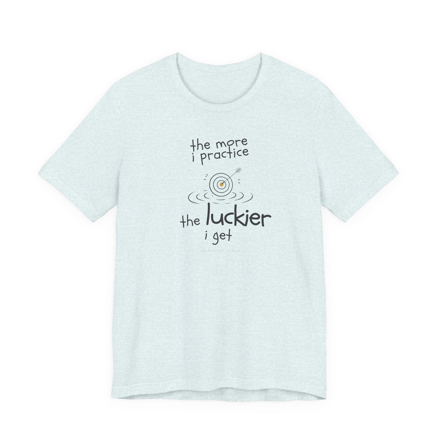 Minimalist motivational T-shirt design shown on a heather ice coloured shirt: hand-drawn cream lettering reads “the more i practice” above a sketched bullseye with an arrow and small mustard center, ripple lines underneath, then larger text reads “the luckier i get” with tiny mono text below that says “repetition > luck.”