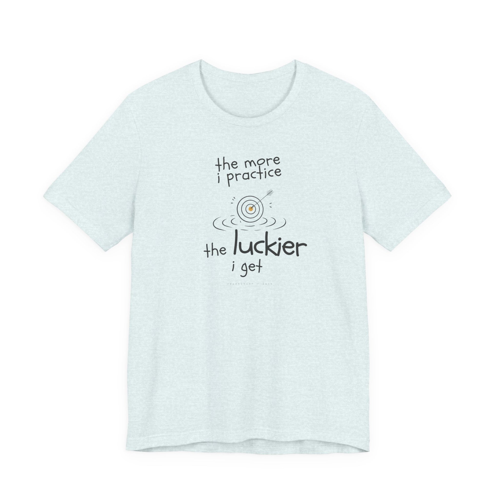 Minimalist motivational T-shirt design shown on a heather ice coloured shirt: hand-drawn cream lettering reads “the more i practice” above a sketched bullseye with an arrow and small mustard center, ripple lines underneath, then larger text reads “the luckier i get” with tiny mono text below that says “repetition > luck.”