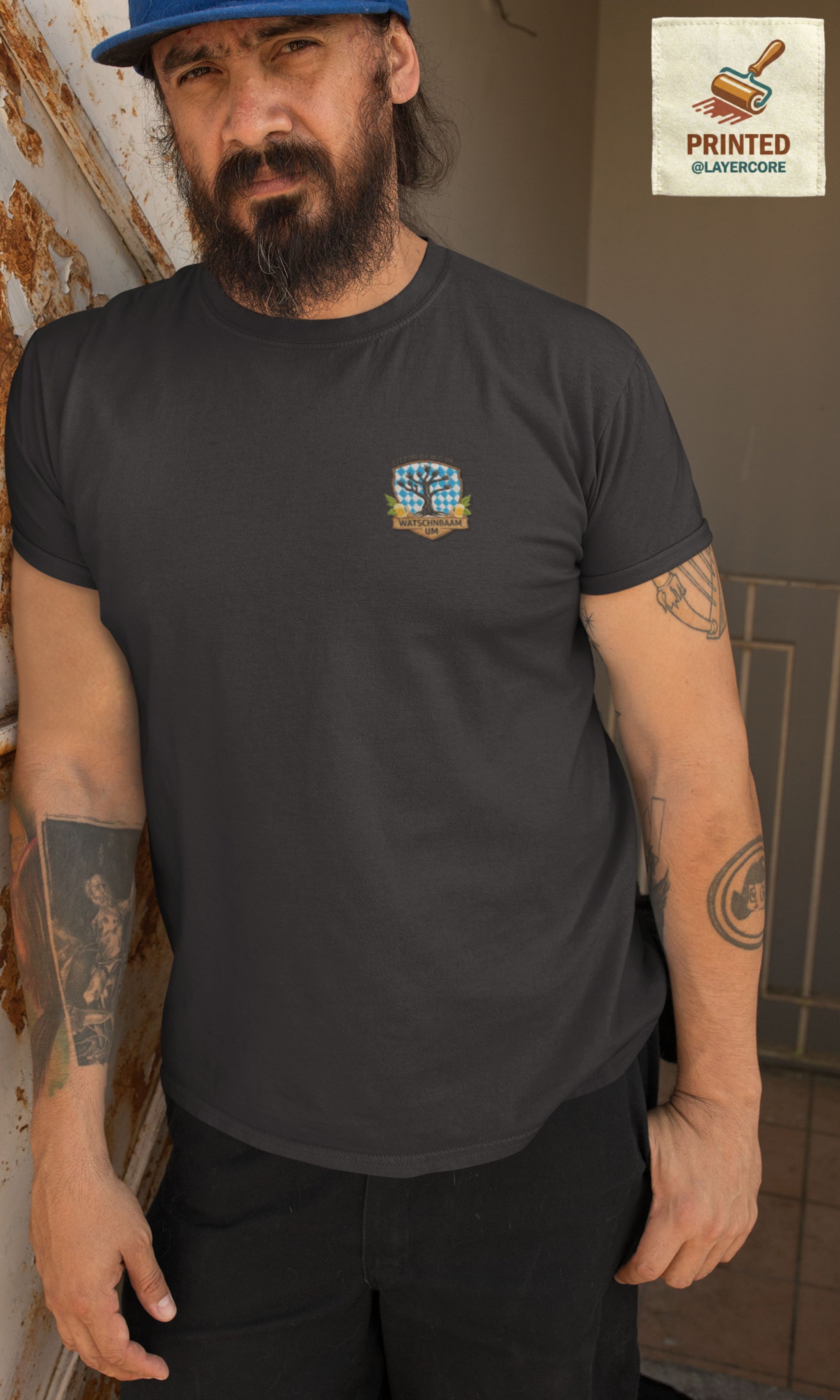 Watschnbaam dunkel graues T-Shirt in Stick-Optik (Druck), bayerisches Wappen mit Händen als Äste, Bierkrügen und Hopfen. Mann mittleren Alters mit Bart und Tattoos trägt das Shirt