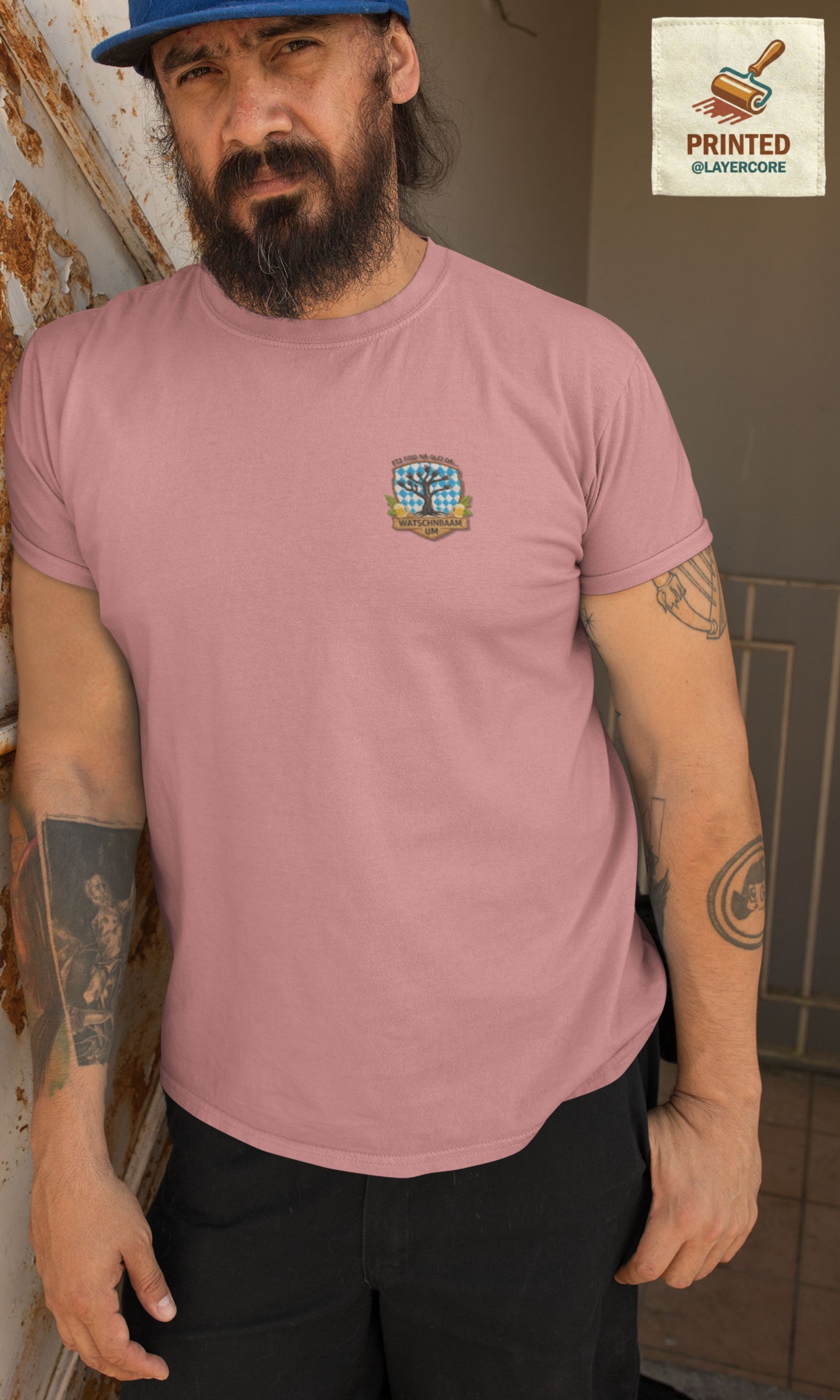 Watschnbaam peach farbenes T-Shirt in Stick-Optik (Druck), bayerisches Wappen mit Händen als Äste, Bierkrügen und Hopfen. Mann mittleren Alters mit Bart und Tattoos trägt das Shirt