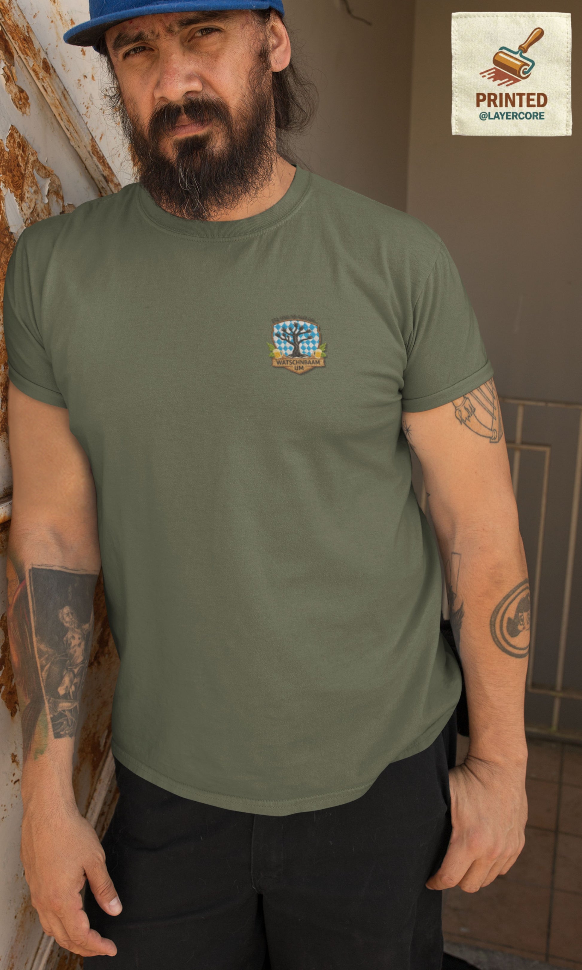 Watschnbaam grünes T-Shirt in Stick-Optik (Druck), bayerisches Wappen mit Händen als Äste, Bierkrügen und Hopfen. Mann mittleren Alters mit Bart und Tattoos trägt das Shirt