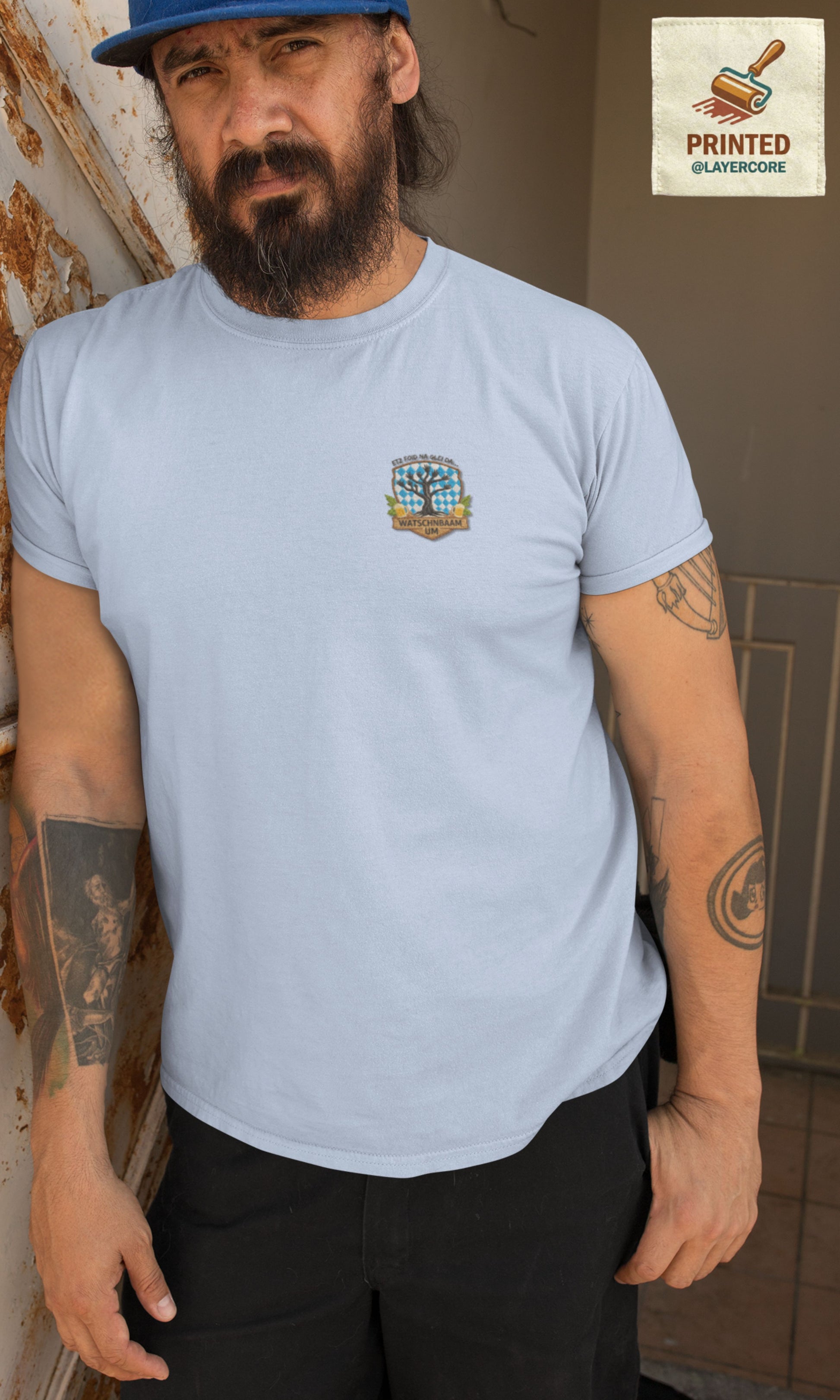 Watschnbaam hellblaues T-Shirt in Stick-Optik (Druck), bayerisches Wappen mit Händen als Äste, Bierkrügen und Hopfen. Mann mittleren Alters mit Bart und Tattoos trägt das Shirt