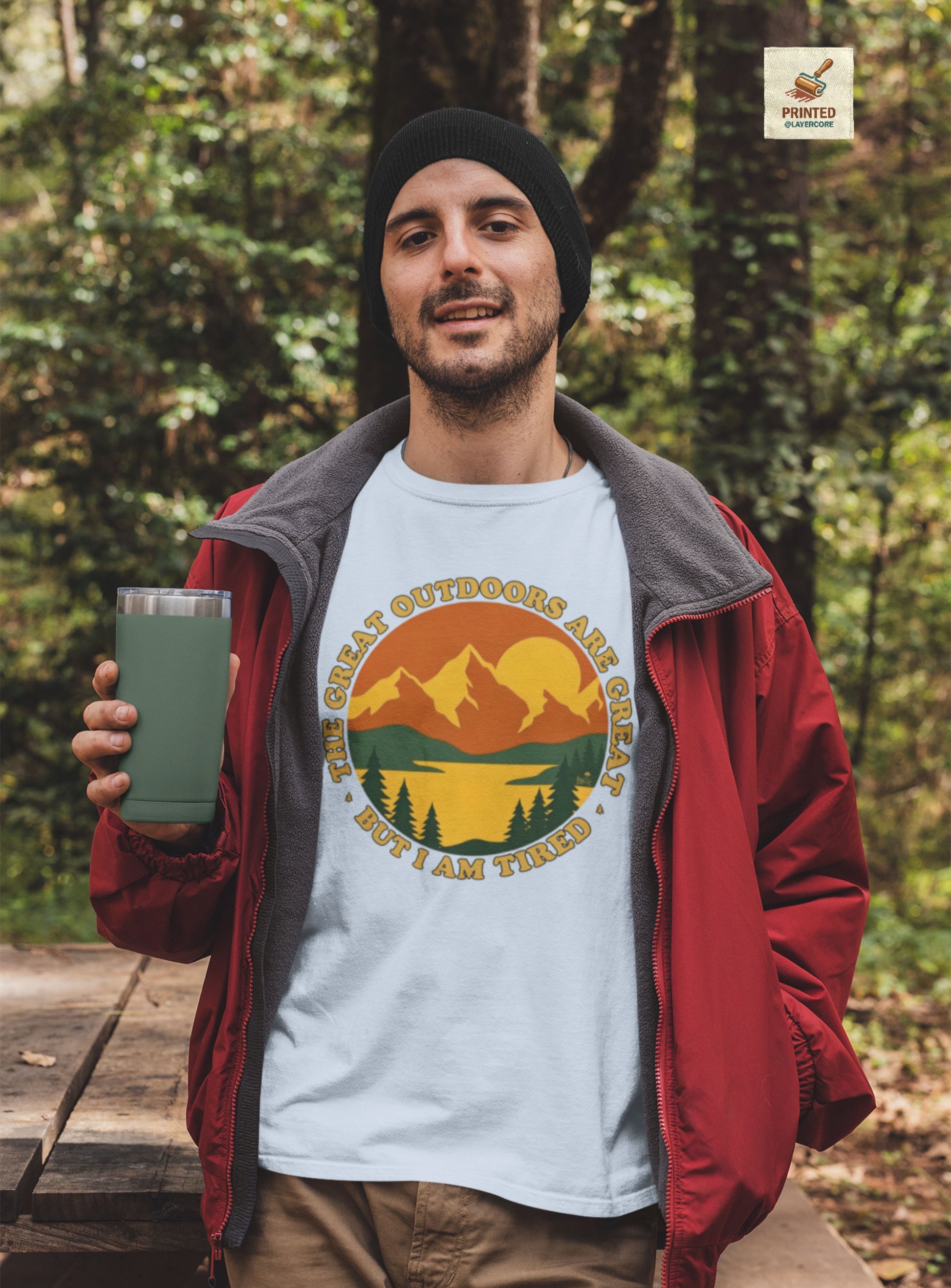 Retro 70s Berglandschaft hellblaues T-Shirt, getargen von einem jungen Mann draußen in der Natur, mit "The Great Outdoors are great but I am tired" Schriftzug.