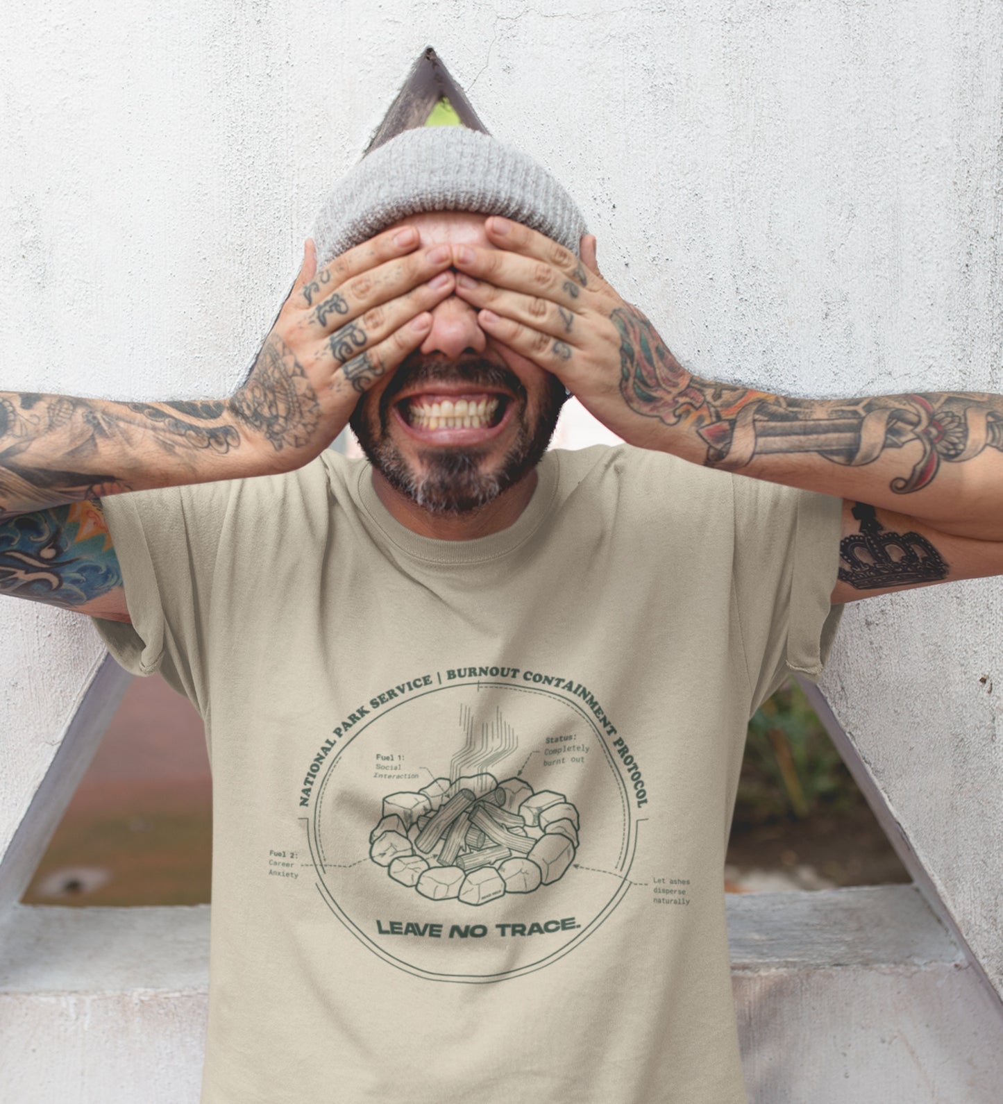 Technisches Diagramm eines Lagerfeuers mit Text Burnout Containment Protocol auf beigem T-Shirt, getragen von einem jungen Mann mit Tattoos. Anti-Gorpcore Streetwear.