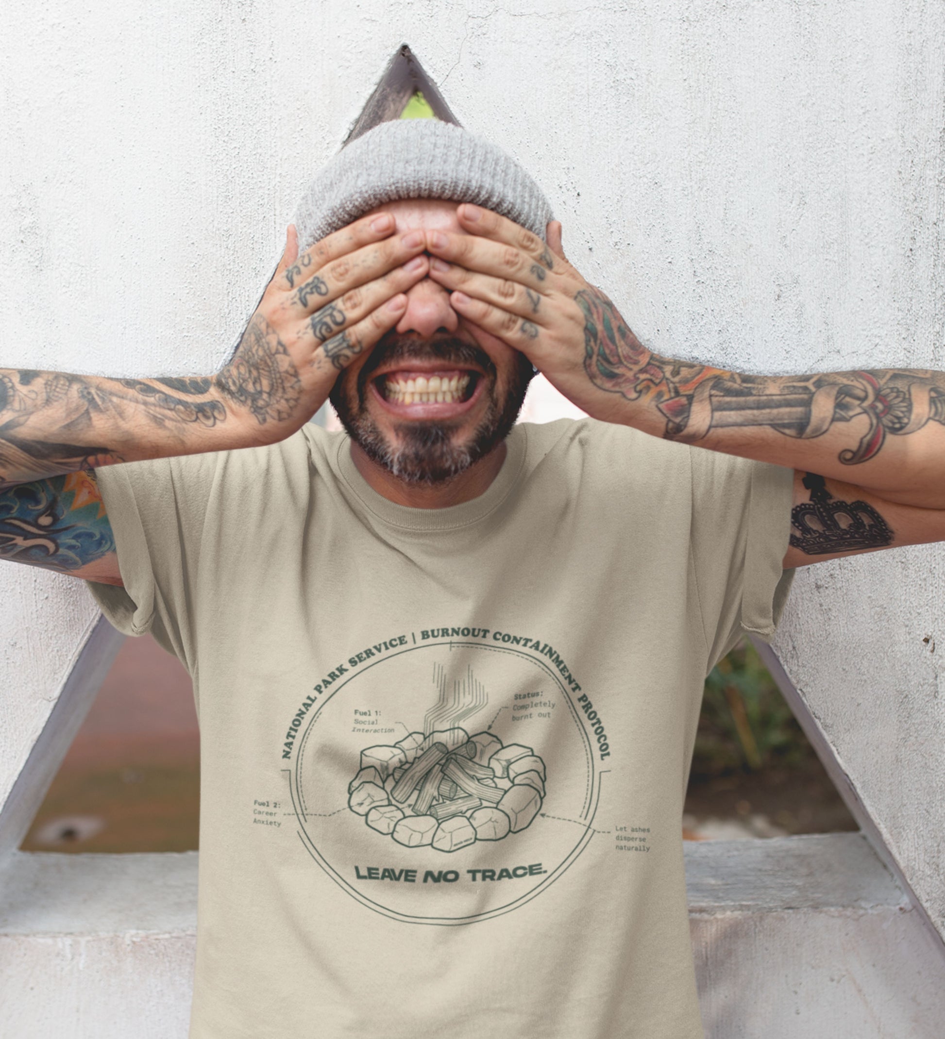 Technisches Diagramm eines Lagerfeuers mit Text Burnout Containment Protocol auf beigem T-Shirt, getragen von einem jungen Mann mit Tattoos. Anti-Gorpcore Streetwear.