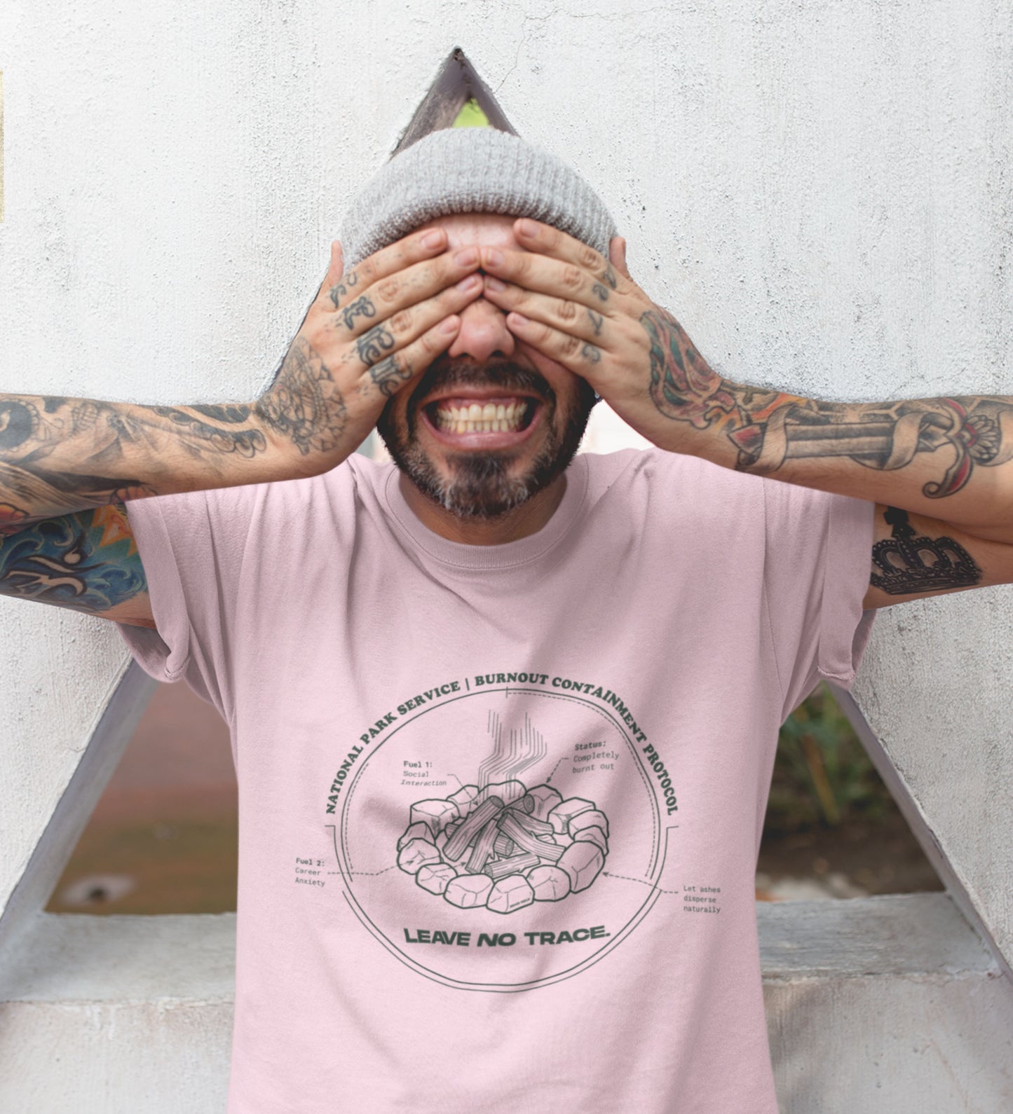 Technisches Diagramm eines Lagerfeuers mit Text Burnout Containment Protocol auf pinkem T-Shirt, getragen von einem jungen Mann mit Tattoos. Anti-Gorpcore Streetwear.