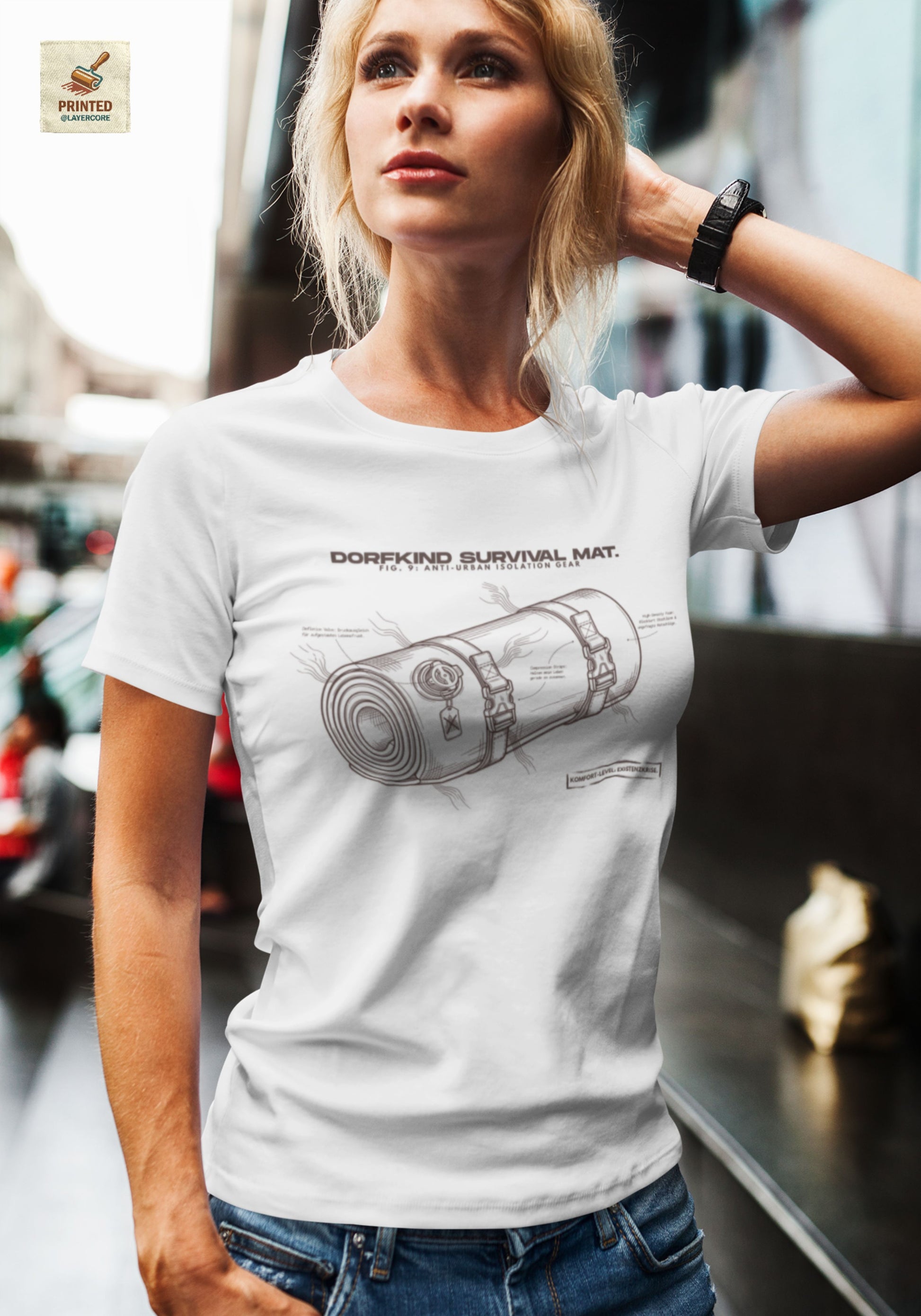 Technische Blueprint-Zeichnung einer Isomatte mit ironischen Texten zum Dorfleben auf einem asche farbenem T-Shirt, getragen von einer jungen Frau. Anti-Gorpcore Design.
