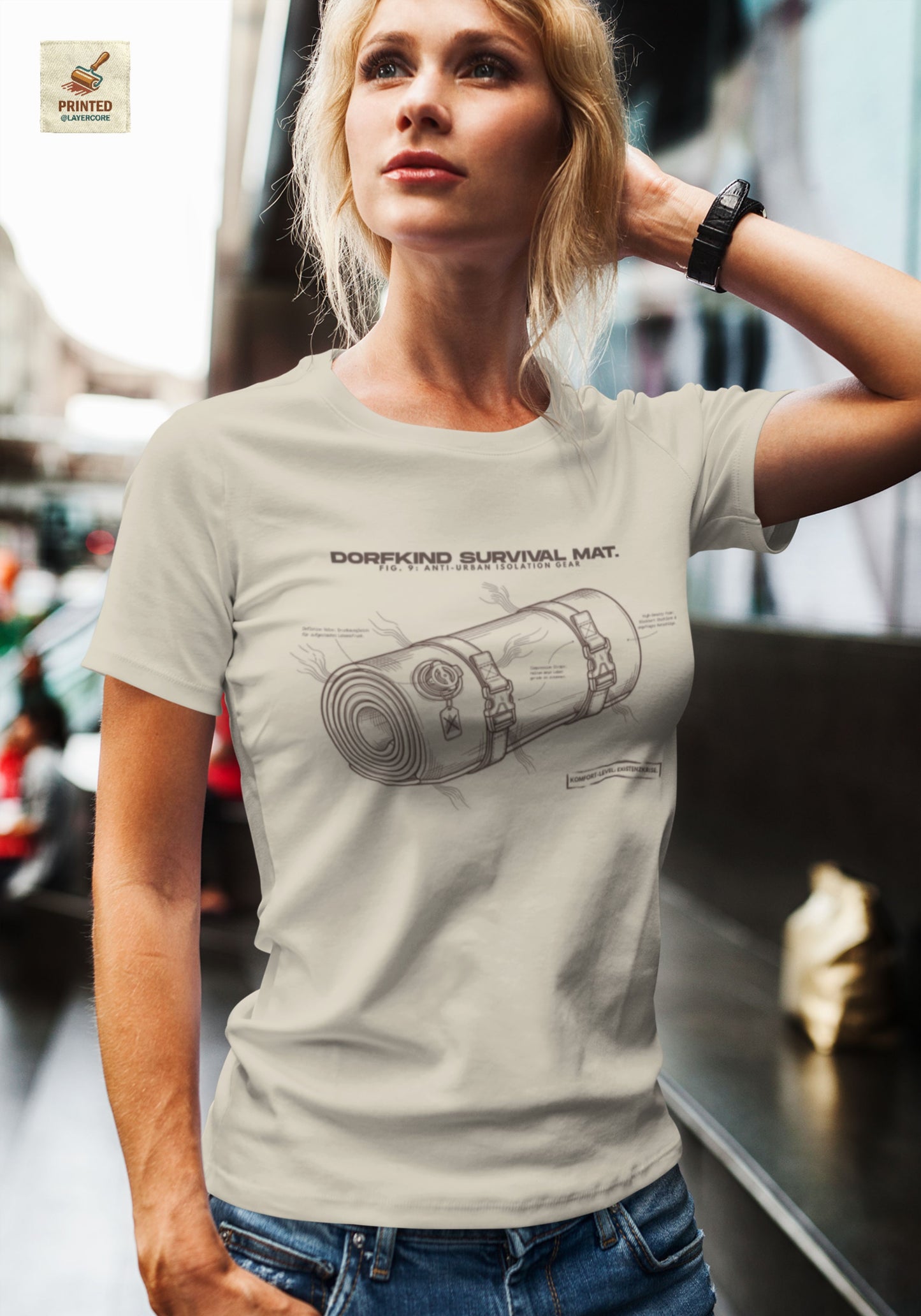 Technische Blueprint-Zeichnung einer Isomatte mit ironischen Texten zum Dorfleben auf einem natural farbenem T-Shirt, getragen von einer jungen Frau. Anti-Gorpcore Design.