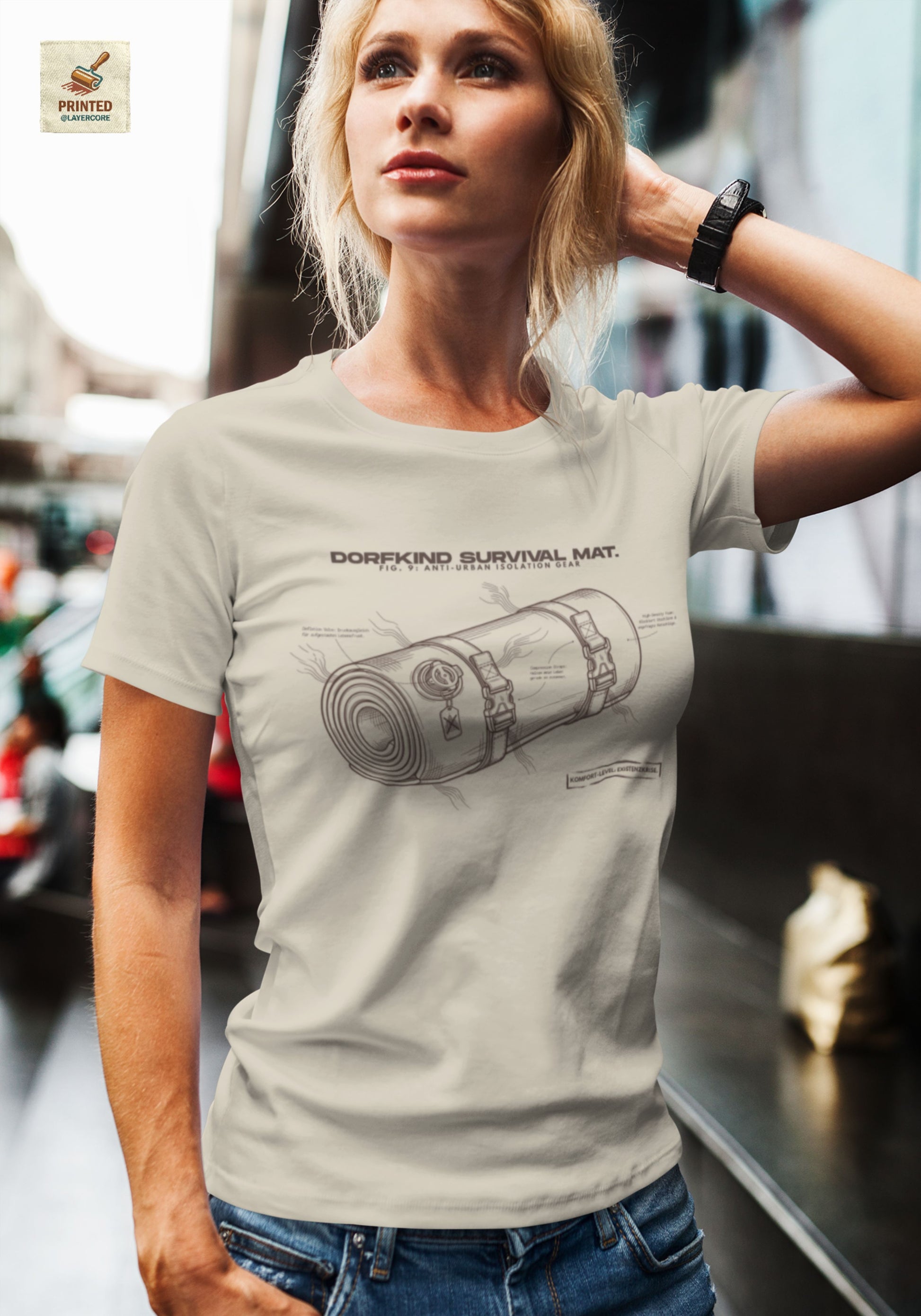 Technische Blueprint-Zeichnung einer Isomatte mit ironischen Texten zum Dorfleben auf einem natural farbenem T-Shirt, getragen von einer jungen Frau. Anti-Gorpcore Design.