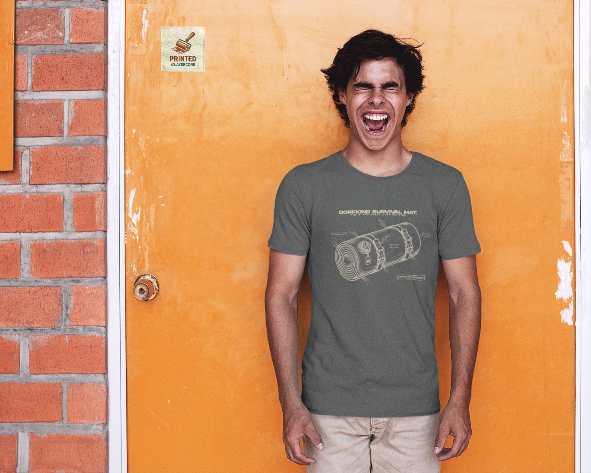 Technische Blueprint-Zeichnung einer Isomatte mit ironischen Texten zum Dorfleben auf einem dark heather farbenem T-Shirt, getragen von einem jungen Mann. Anti-Gorpcore Design.