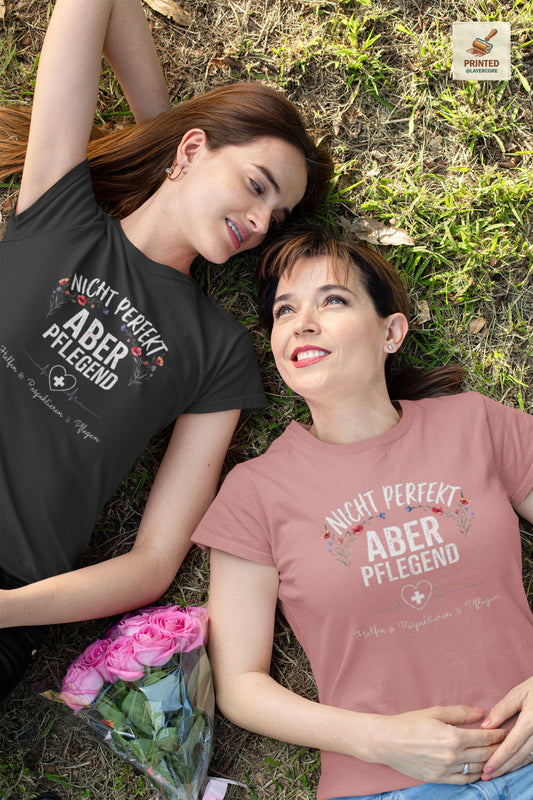 T-Shirt Nicht perfekt aber pflegend mit Blumenkranz und EKG Herz für Krankenschwestern und Pflegekräfte im Schichtdienst, getragen von zwei Frauen, welche auf einer Wiese liegen