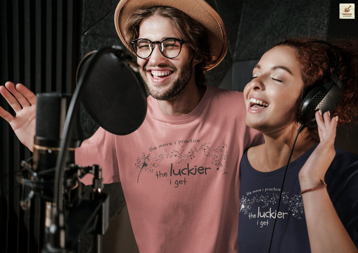 Front view of a blue and mauve Bella Canvas t-shirt with a clever music-themed graphic, worn by two young people. The design shows a stylized guitar headstock and musical notes above text that reads: ‘The more I practice, the luckier I get.’ Soft 100% cotton shirt perfect for musicians and music teachers.