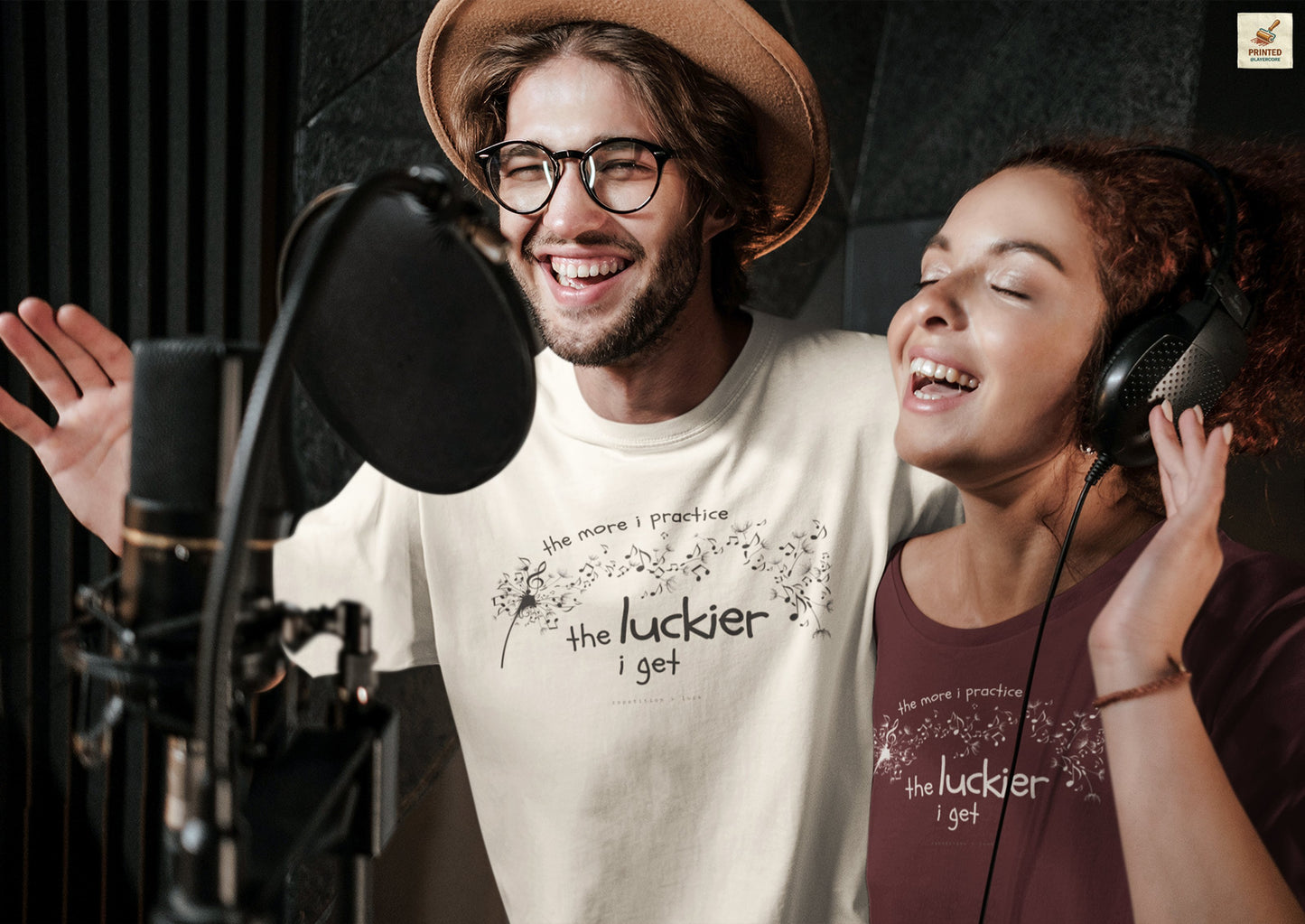 Front view of a natural coloured and maroon Bella Canvas t-shirt with a clever music-themed graphic, worn by two young people. The design shows a stylized guitar headstock and musical notes above text that reads: ‘The more I practice, the luckier I get.’ Soft 100% cotton shirt perfect for musicians and music teachers.