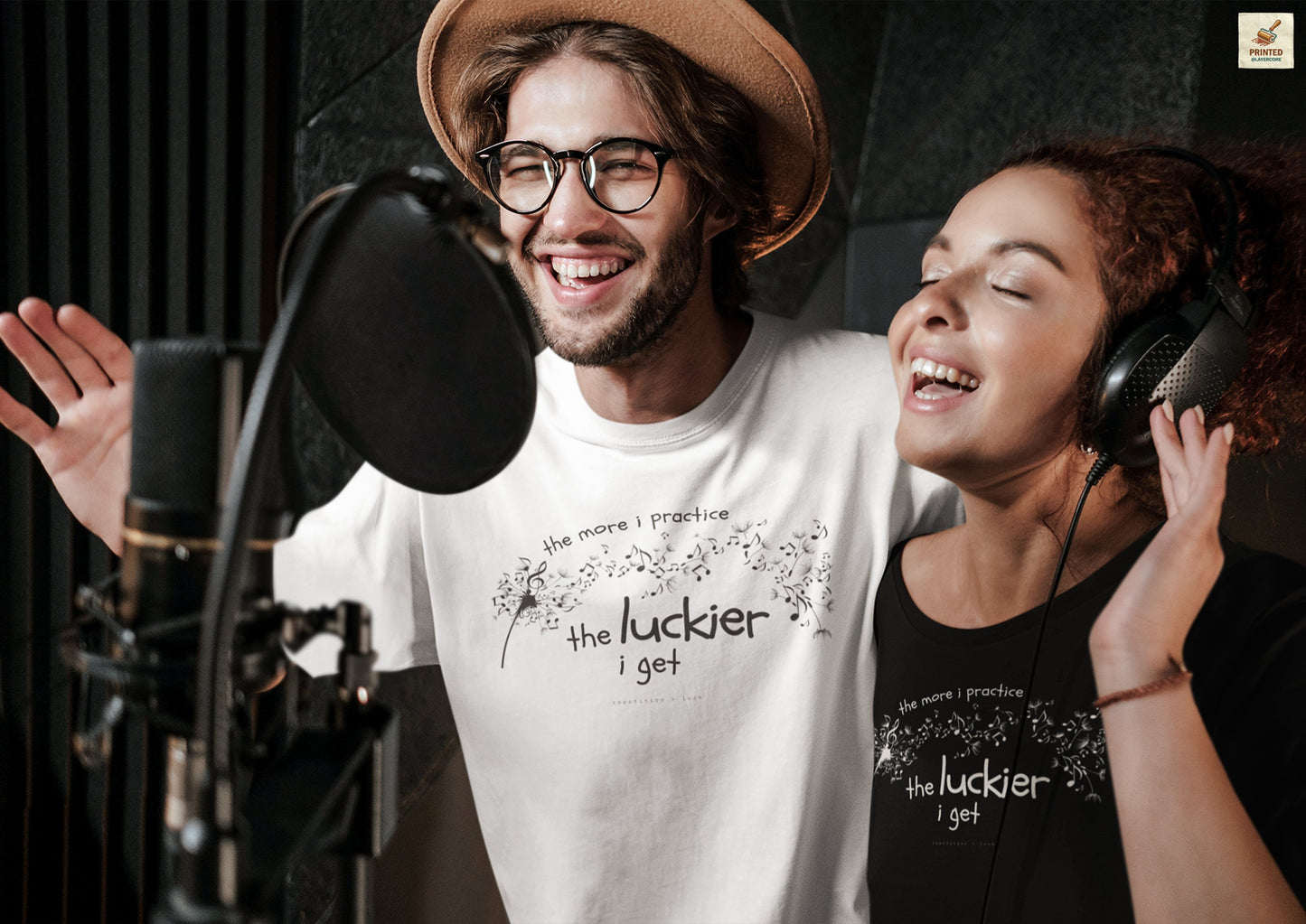 Front view of a white and black Bella Canvas t-shirt with a clever music-themed graphic, worn by two young people. The design shows a stylized guitar headstock and musical notes above text that reads: ‘The more I practice, the luckier I get.’ Soft 100% cotton shirt perfect for musicians and music teachers.