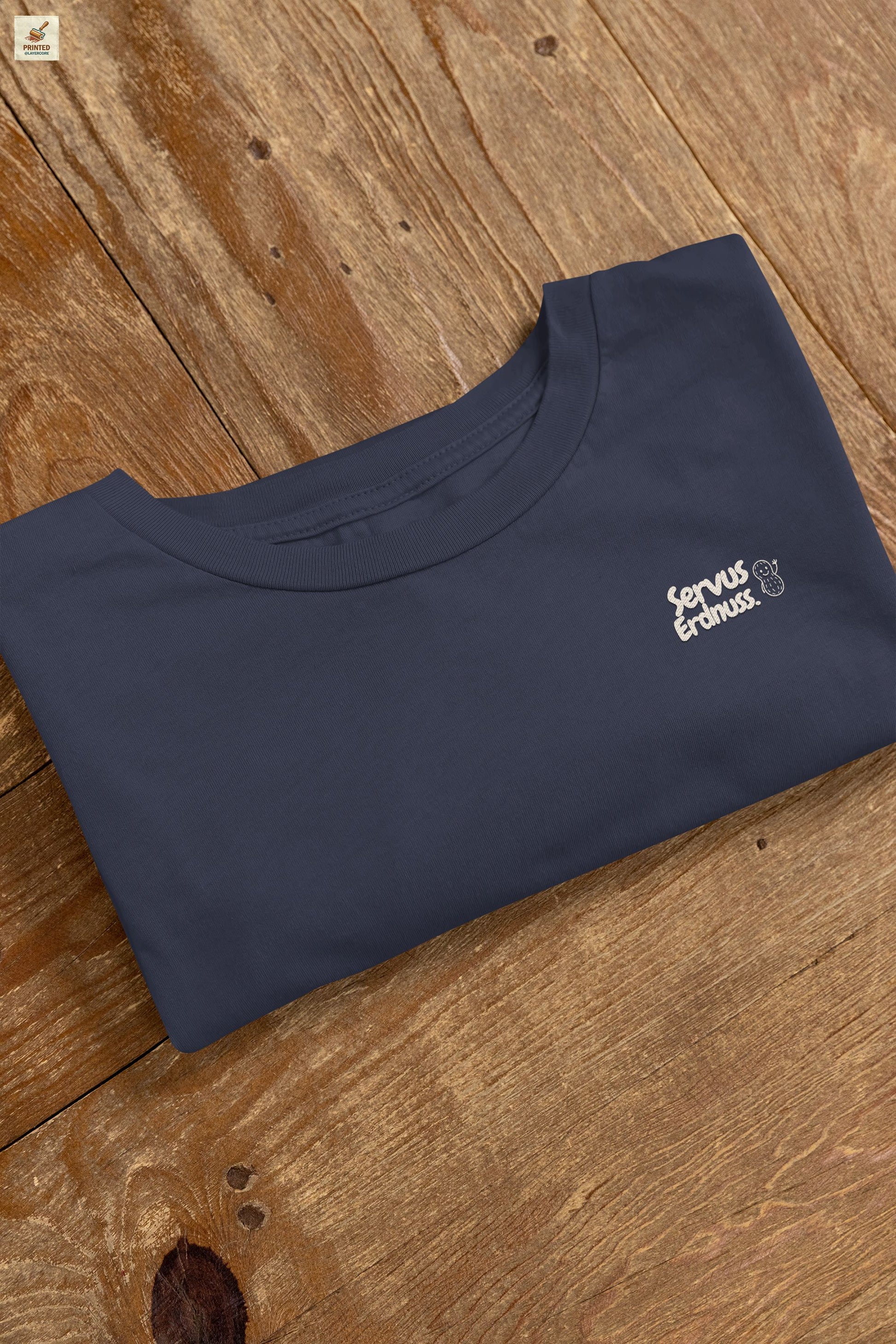 Servus Erdnuss Brustmotiv mit Dialekt-Text und kleiner Erdnussfigur auf navyblauem Shirt
