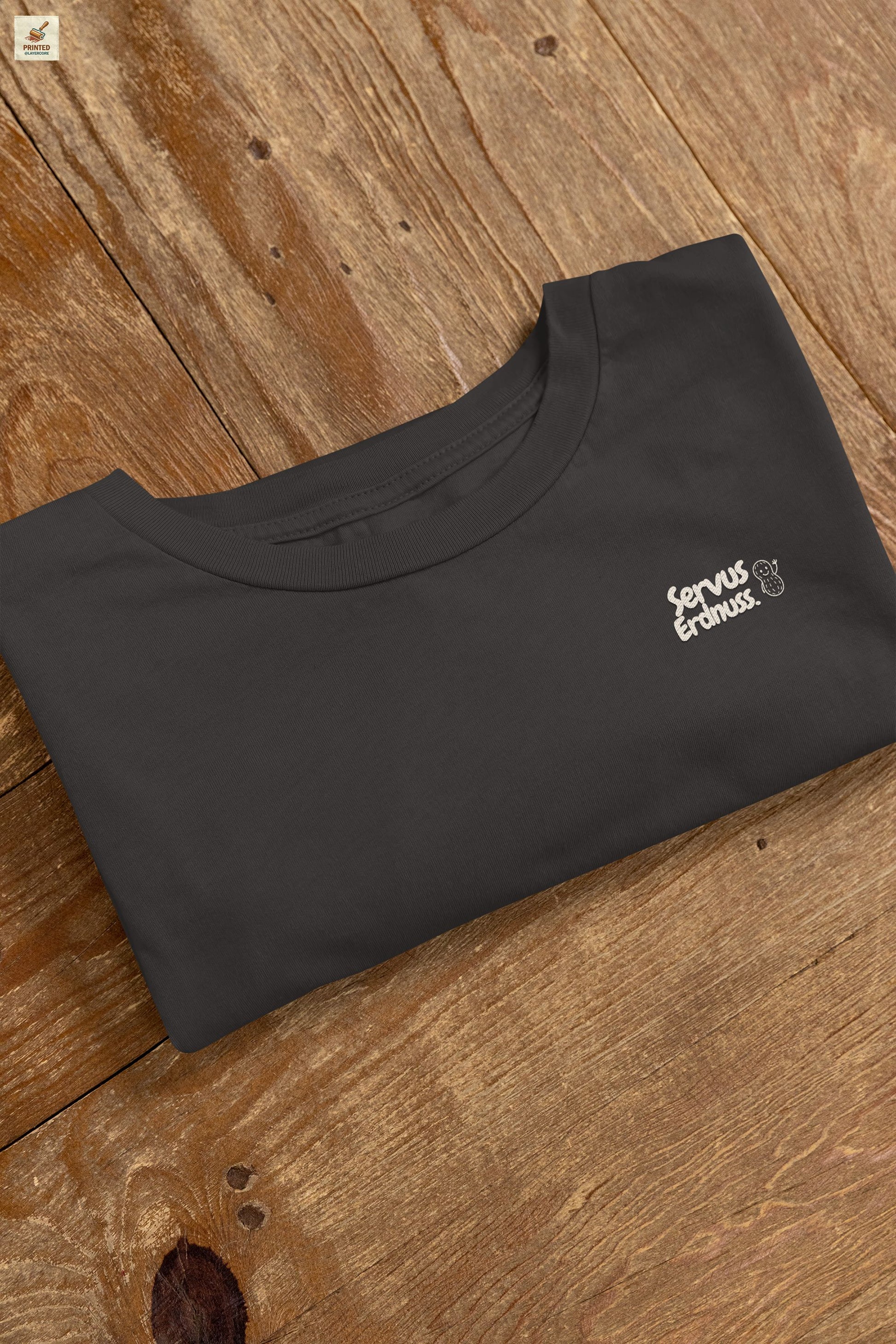 Servus Erdnuss Brustmotiv mit Dialekt-Text und kleiner Erdnussfigur auf dunkelgrauem Shirt