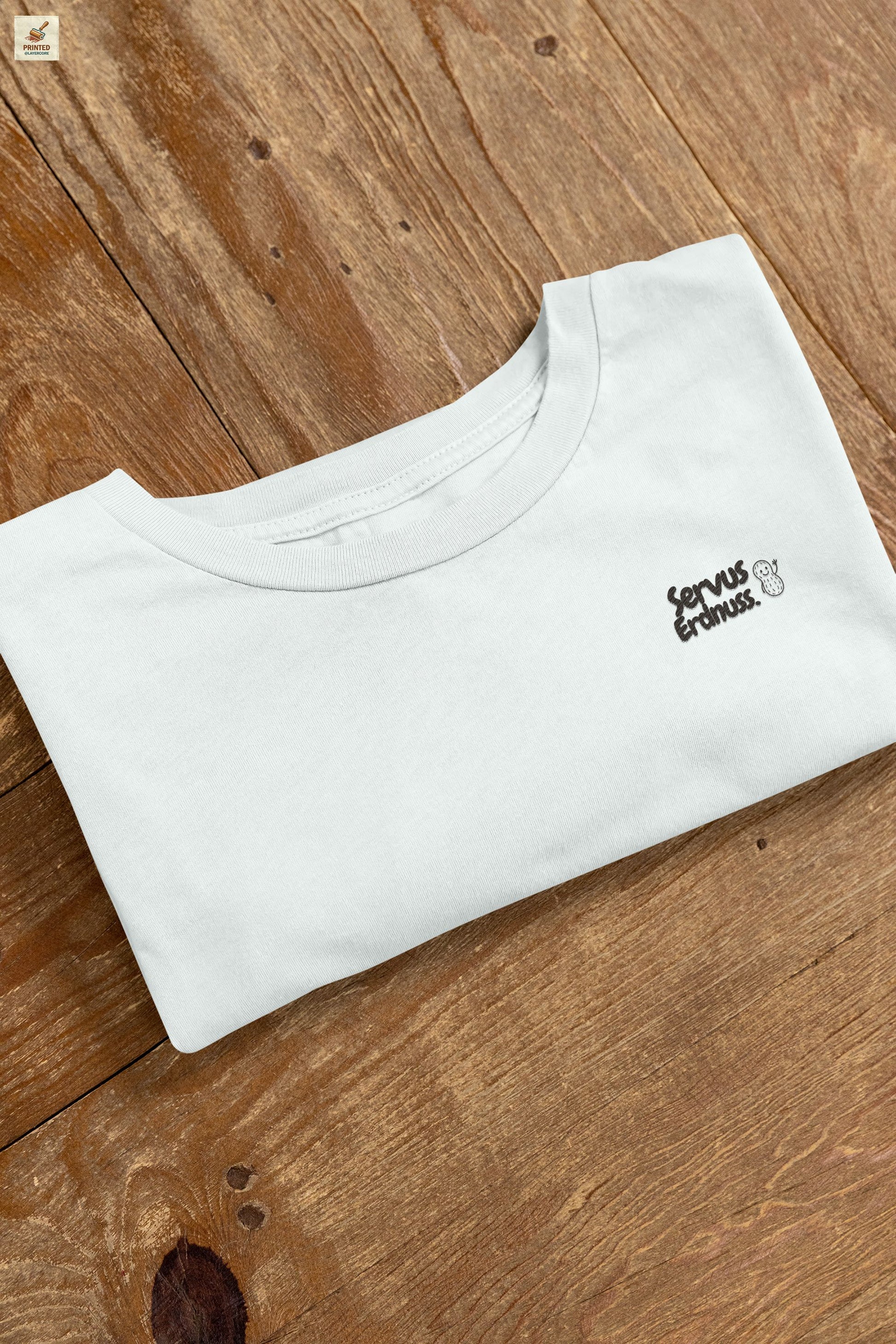 Servus Erdnuss Brustmotiv mit Dialekt-Text und kleiner Erdnussfigur auf heather ice blue farbenem Shirt