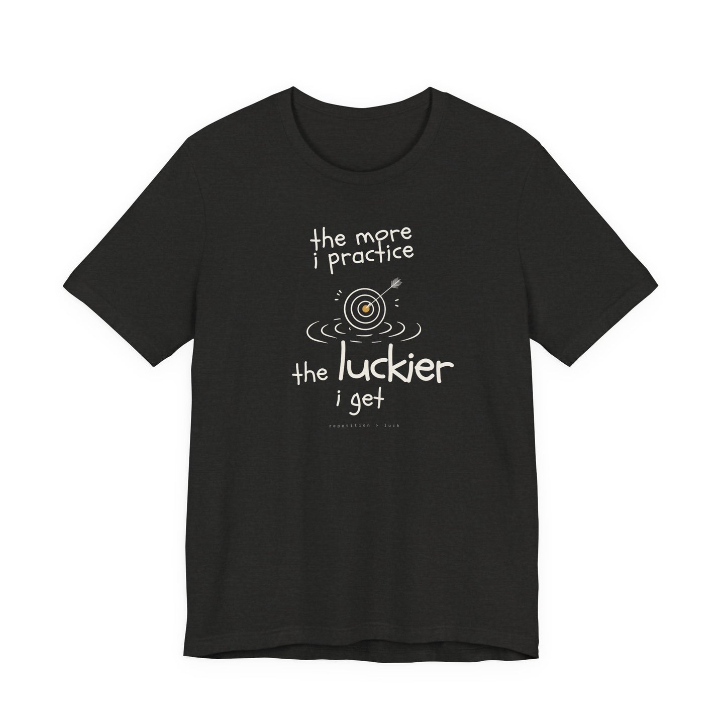 Minimalist motivational T-shirt design shown on a black shirt: hand-drawn cream lettering reads “the more i practice” above a sketched bullseye with an arrow and small mustard center, ripple lines underneath, then larger text reads “the luckier i get” with tiny mono text below that says “repetition > luck.”