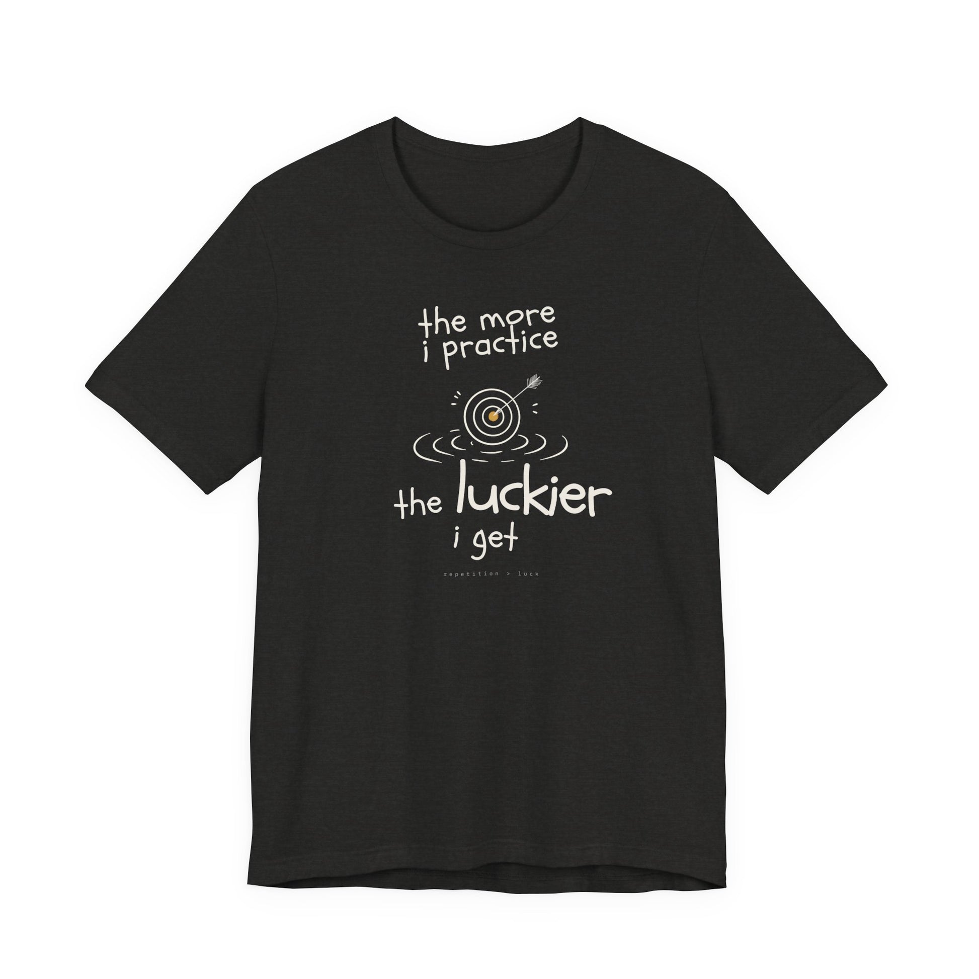 Minimalist motivational T-shirt design shown on a black shirt: hand-drawn cream lettering reads “the more i practice” above a sketched bullseye with an arrow and small mustard center, ripple lines underneath, then larger text reads “the luckier i get” with tiny mono text below that says “repetition > luck.”