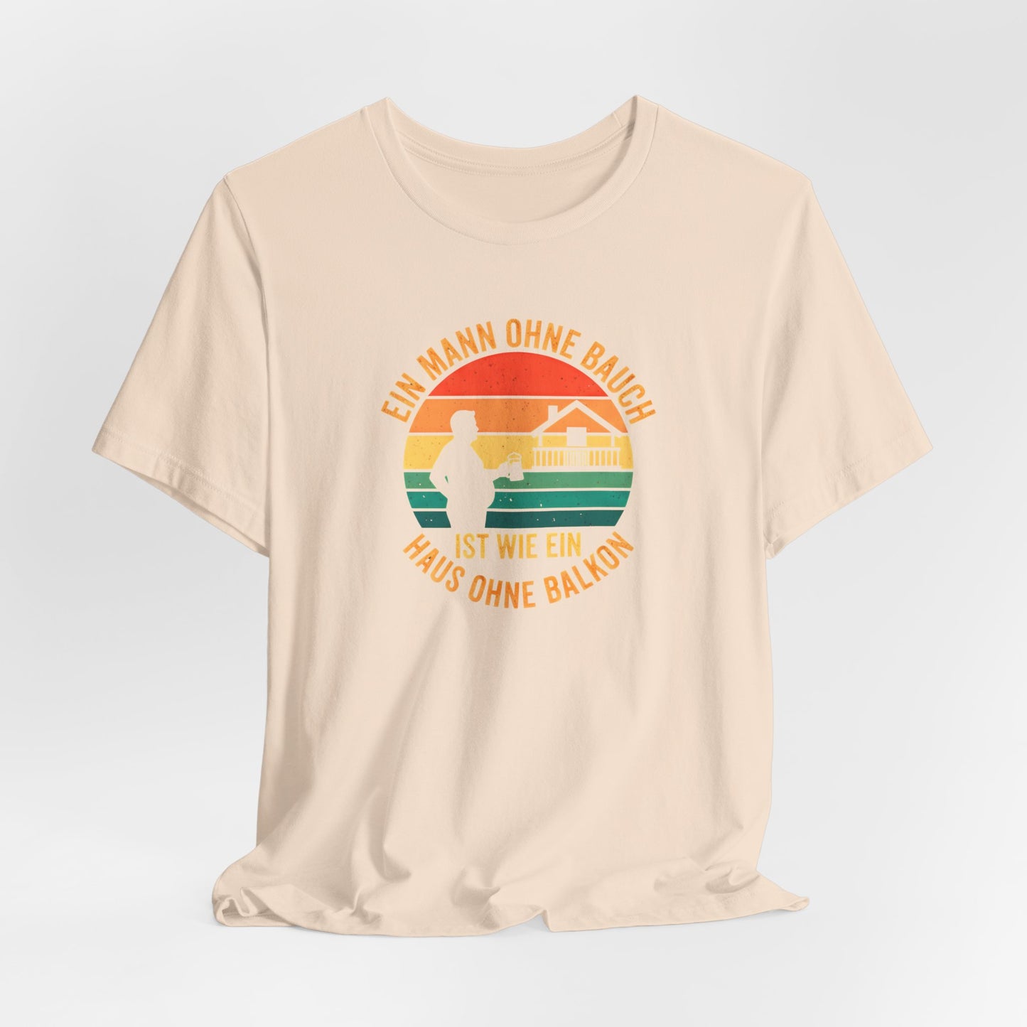 Nahaufnahme des hochwertigen Textildrucks auf dem sandfarbenem T-Shirt. Das runde Retro-Design zeigt die Silhouette eines Mannes mit Bierkrug neben einem Haus mit prominentem Balkon vor einem gestreiften Sonnenuntergang. Der Text "EIN MANN OHNE BAUCH IST WIE EIN HAUS OHNE BALKON" umrahmt das Motiv in einer Vintage-Schriftart. Der Druck ist scharf, die Farben sind deckend, aber nicht gummiartig, was auf eine hohe Qualität hindeutet. Man erkennt die weiche Textur der Baumwolle des Bella Canvas 3001 Shirts.