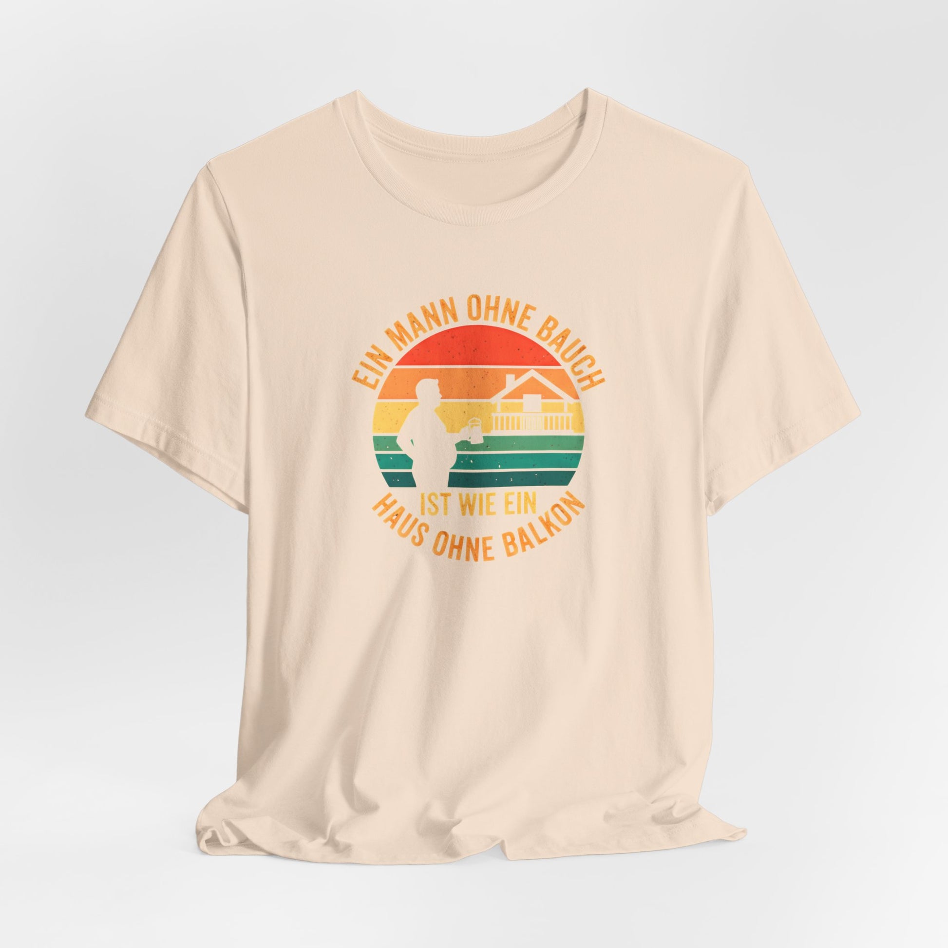 Nahaufnahme des hochwertigen Textildrucks auf dem sandfarbenem T-Shirt. Das runde Retro-Design zeigt die Silhouette eines Mannes mit Bierkrug neben einem Haus mit prominentem Balkon vor einem gestreiften Sonnenuntergang. Der Text "EIN MANN OHNE BAUCH IST WIE EIN HAUS OHNE BALKON" umrahmt das Motiv in einer Vintage-Schriftart. Der Druck ist scharf, die Farben sind deckend, aber nicht gummiartig, was auf eine hohe Qualität hindeutet. Man erkennt die weiche Textur der Baumwolle des Bella Canvas 3001 Shirts.