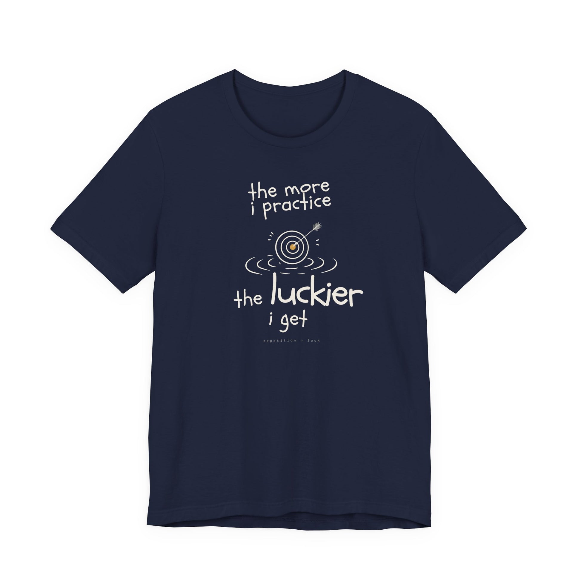 Minimalist motivational T-shirt design shown on a dark blue shirt: hand-drawn cream lettering reads “the more i practice” above a sketched bullseye with an arrow and small mustard center, ripple lines underneath, then larger text reads “the luckier i get” with tiny mono text below that says “repetition > luck.”